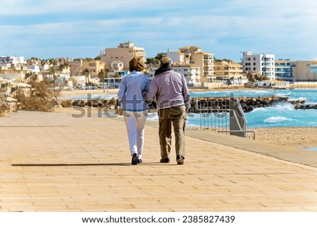 elderly man and woman dressed warmly walk along the promenade of Palma de Mallorca in late fall