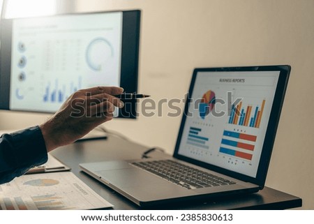 Young Asian businessman working with laptop, checking graphs, company budget reports, production control. Operational inspection cost plus price Close-up pictures Royalty-Free Stock Photo #2385830613