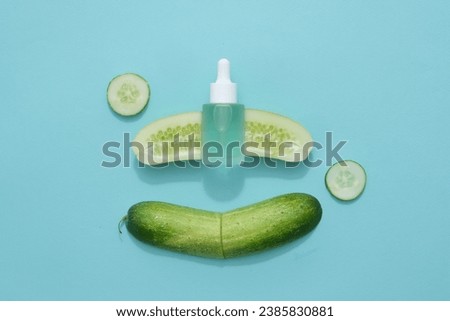 A blue glass dropper bottle unbranded mockup for design, placed on fresh cucumber slices on pastel blue background. Advertising scene for cosmetic from cucumber ingredient