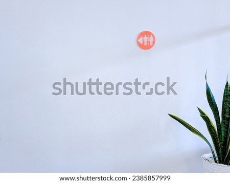 A potted plant next to a bathroom sign on a white wall.