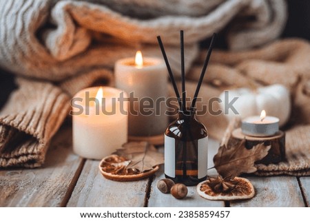 Hello autumn, cozy slow living. Pumpkin, aromatic candle, warm sweaters, dry fall leaves, cinnamon, anise in golden lights with bokeh on white wooden background. Thanksgiving apartment decor Royalty-Free Stock Photo #2385859457