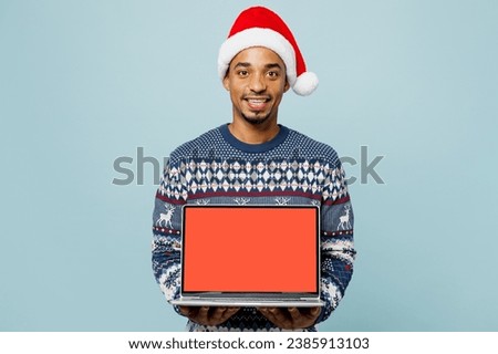 Young IT man wear sweater Santa hat posing hold use work on blank screen workspace area laptop pc computer isolated on plain blue background. Happy New Year 2024 celebration Christmas holiday concept