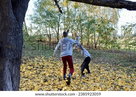 Two boys are playing with yellow autumn leaves under a tree in the garden.
