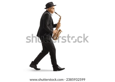Full length profile shot of a man walkign and playing a sax isolated on white background Royalty-Free Stock Photo #2385932599
