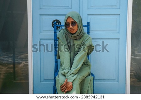 Beautiful Muslim woman in hijab sitting on a chair wearing a green dress and glasses