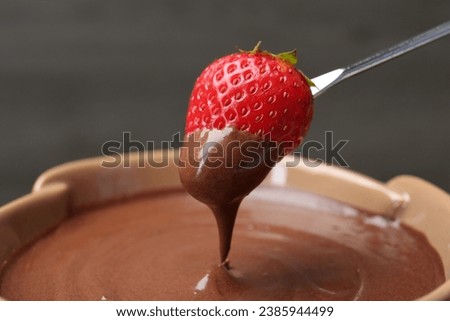 Strawberry with melted chocolate on fork above fondue, closeup. Space for text Royalty-Free Stock Photo #2385944499