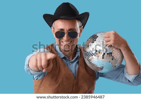 Cool mature cowboy with disco ball pointing at viewer on blue background, closeup