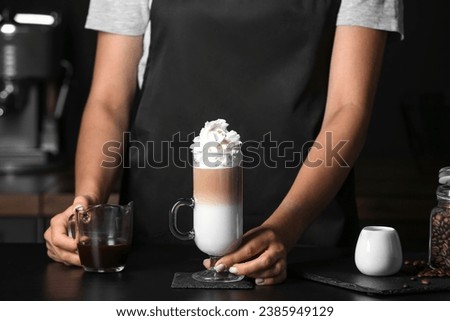 Barista holding glass of tasty latte with whipped cream in cafe Royalty-Free Stock Photo #2385949129