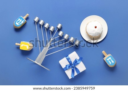 Hannukah composition with menorah, dreidels, gift box and donut on blue background Royalty-Free Stock Photo #2385949759