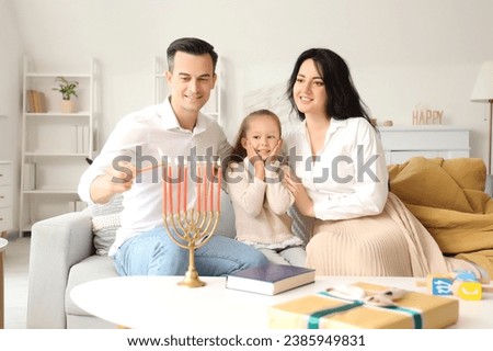 Happy family lighting candles for Hanukkah at home Royalty-Free Stock Photo #2385949831