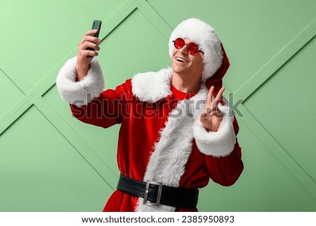 Santa Claus showing victory gesture and taking selfie on green background