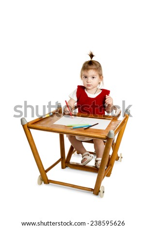 Little girl sitting at the table and draws a pencil and looking at the camera isolated on a white background