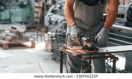 Polishing the surface with angle grinder. Close up view of man that is working at the factory. Royalty-Free Stock Photo #2385965229