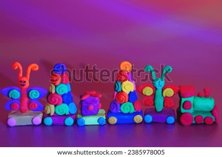A toy Christmas train made of plasticine with gifts and Christmas trees. Bright purple background. New Year decorations.