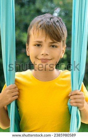 Preteen boy in air yoga hammock looking at camera. Child exercise in park outside. Flexibility and mental harmony for children. Fresh air sport Healthy activity for kids