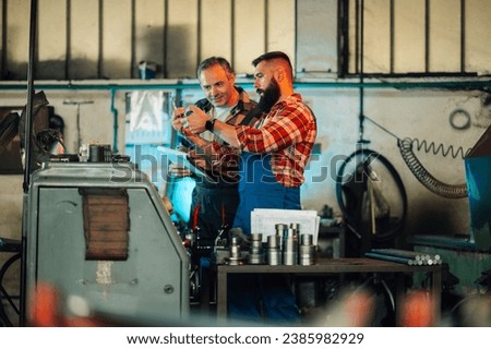 A picture of two factory workers, metal turners, looking at a newly produced metal roll cut piece. The senior supervisor engineer is holding a clipboard, curiously checking the piece. Lathe machine.