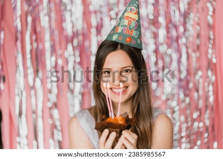Beautiful girl smiling at her birthday party holding a cake with tree candles happy with hat on the heady  Royalty-Free Stock Photo #2385985567