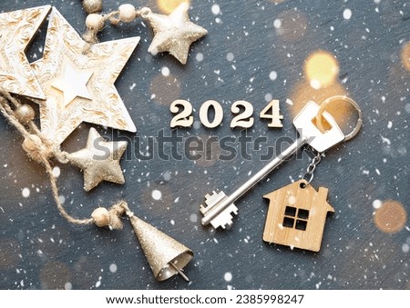 House key with keychain cottage on festive background with stars, lights of garlands. New Year 2024 wooden letters, greeting card. Purchase, construction, relocation, mortgage, insurance