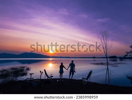 Photo silhouette scene, man, woman, travel couple stand and holding hands watch sunset at last light on New Year's Eve, enjoy relax in vacation. Romantic on holiday at lake in Huai Mai Teng, Thailand.