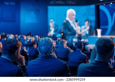 Businessmen listening to director giving presentation on projection screen at export forum Royalty-Free Stock Photo #2385999259