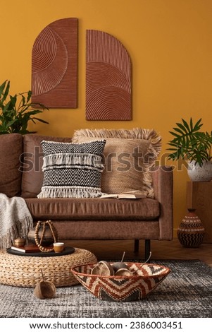 Interior design of warm and cozy living room interior with brown sofa, yellow wall, braided pouf, vase with leaves, books, patterned carpet and personal accessories. Home decor. Template. Royalty-Free Stock Photo #2386003451