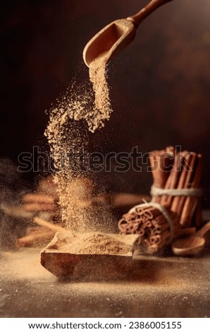 Cinnamon powder is poured into a wooden bowl. In the background are kitchen utensils and cinnamon sticks. Royalty-Free Stock Photo #2386005155