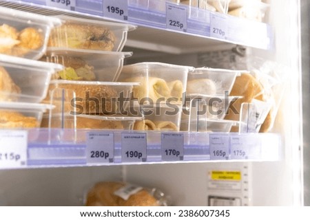 Close-up view of various prepared food lying on fridge shelf in micro market (small unattended vending store). Prepared food theme. Russian text translation: Chicken bagel and Pancakes with meat. Royalty-Free Stock Photo #2386007345
