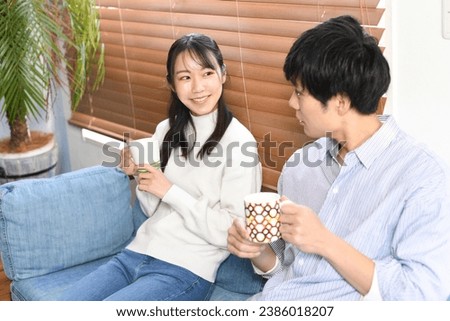 A young Asian couple holding a cup and having a conversation while sitting on the sofa at home
 Royalty-Free Stock Photo #2386018207