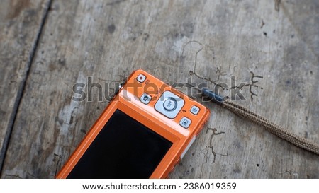 Orange digital camera on a wooden board background