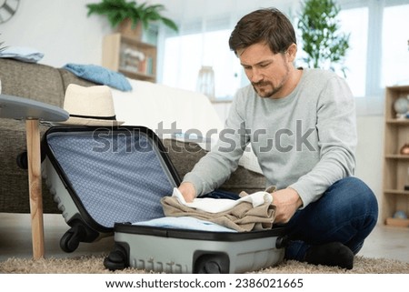 young smiling man packing clothes into travel bag Royalty-Free Stock Photo #2386021665