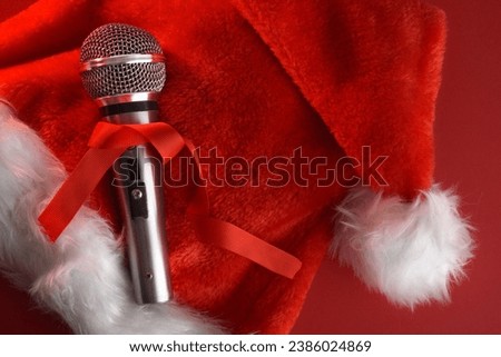 Detail of christmas musical background with metallic stage microphone with red bow on santa hat isolated on red background. Top view.