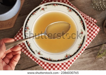 Chicken bone broth or soup on a spoon held by a hand above a plate