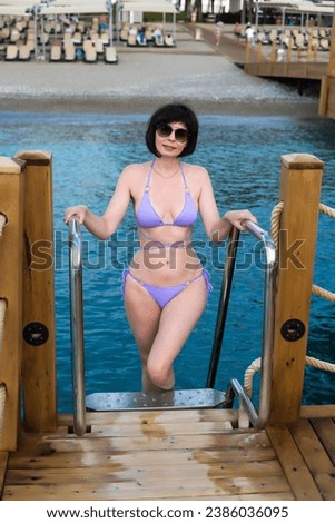 A slender brunette woman rises from the sea along the stairs to the pier.