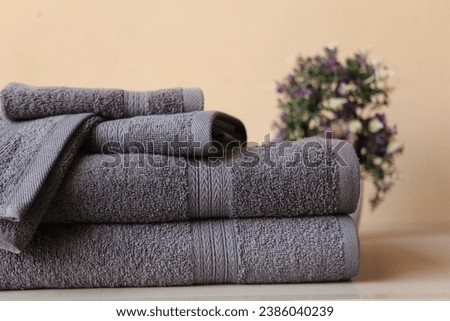 Stack of 2 Arrow Fancy Grey Bath Towels, 1 Hand Towel, and 2 Wash Cloths, Isolated on a Beige Background with a Blurred Backdrop Featuring Lush Plants Royalty-Free Stock Photo #2386040239