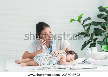 an Asian mother talking on mobile phone. to greet with others while her 7-month-old daughter was sleeping with smile and happy, to family and infant newborn concept.