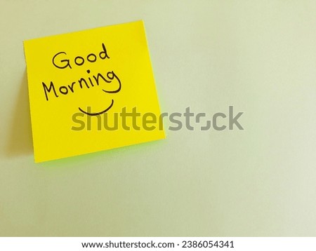 Message written on a yellow sticky note, 'Good morning', on blank sheet of white paper with copy space