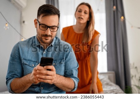 Jealous woman spying boyfriend and watching his mobile phone. Couple cheating jealousy concept Royalty-Free Stock Photo #2386055443