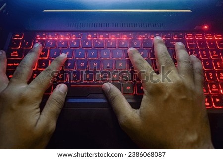 hands typing on a gaming laptop keyboard that glows red