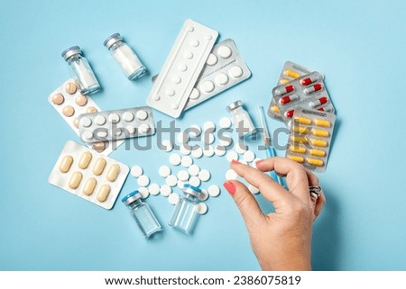 Hand holding one white pill on blue background full of colorful pills and medicines Royalty-Free Stock Photo #2386075819