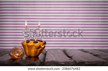 Birthday number 98. Date of birth with number of candles, copy space. Anniversary background with cake or muffin with burning candles. Greeting card.