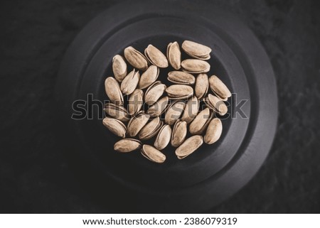 Elegant jet-black plate adorned with luscious pistachios, placed on a glossy black surface. A captivating play of shadows and highlights, perfect for gourmet concepts.