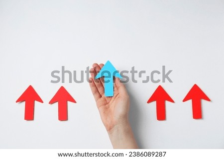 Woman holding light blue paper arrow among red arrows on white background, top view. Space for text