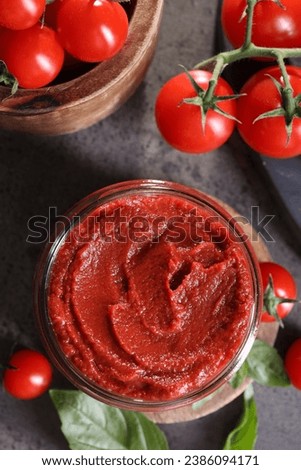 Jar of tasty tomato paste and ingredients on grey textured table, flat lay