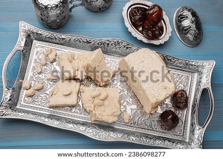 Pieces of tasty halva, dates and peanuts served in vintage tea set on light blue wooden table, above view