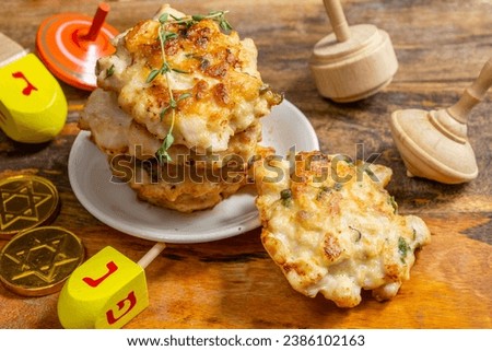 Chicken fritters or latkes, wooden dreidel for Jewish holiday Hanukkah. Hebrew letters on dreidels say: "Great Miracle Happened Here".  Royalty-Free Stock Photo #2386102163