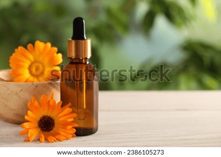 Bottle of essential oil and beautiful calendula flowers on white wooden table outdoors, closeup .Space for text