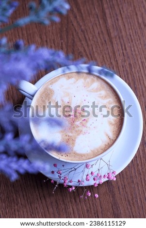 Top view of a cup of aromatic hot coffee on the table, romantic card, bouquet of lilac flowers in blur, weekend morning mood, breakfast ritual, laconic photo in flatlay style, table surface