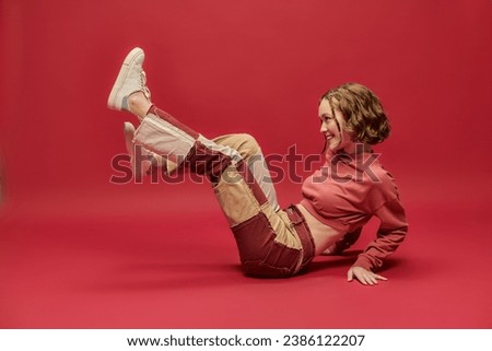 self-expression, joyful woman in patchwork pants and cropped long sleeve sitting on red backdrop Royalty-Free Stock Photo #2386122207