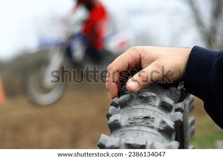 Dirt bike race racing. Extreme sports. Motocross. Man's hand on old knubby bumpy tire. Spectator watching races. Selective focus. Blurred background man riding dirtbike. Competition. Track. Course.