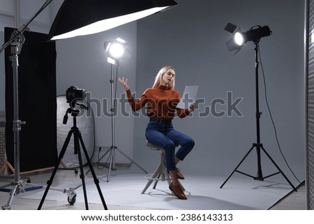 Casting call. Emotional woman with script sitting on chair and performing in front of camera in studio Royalty-Free Stock Photo #2386143313